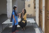 Индийская девушка рядом с молодой взрослой женщиной разговаривает по мобильному телефону, сидя на койке — стоковое фото