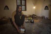 Mujer india sentada en la cocina y cocinando comida en leña con utensilios - foto de stock