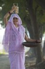 Donna indiana che trasporta scatola tiffin sulla testa e padella in oro ferro in mano — Foto stock