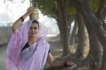 Mujer india que lleva la caja de tiffin en la cabeza y pan de oro de hierro en la mano - foto de stock