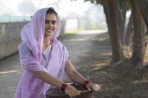 Smiling young adult woman in sari carrying iron gold pan in hand — Stock Photo
