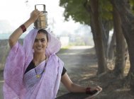 Donna indiana che trasporta scatola tiffin sulla testa e padella in oro ferro in mano — Foto stock