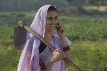 Портрет улыбающейся женщины, несущей лопату на плече и разговаривающей по мобильному телефону — стоковое фото