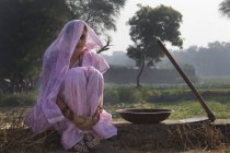 Жінка в рожевому сарі сидить біля сільськогосподарського поля — стокове фото