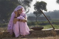 Женщина в розовом сари сидит рядом с сельскохозяйственным полем — стоковое фото