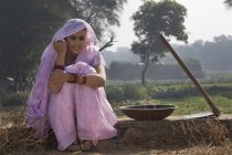 Frau im rosafarbenen Sari sitzt in der Nähe eines landwirtschaftlichen Feldes — Stockfoto