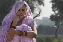 Портрет жінки в рожевому сарі, що сидить біля сільськогосподарського поля — стокове фото