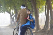 Visão traseira da estudante feliz andando de bicicleta com o pai na aldeia — Fotografia de Stock