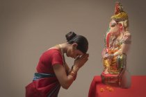 Mujer rezando con las manos unidas y los ojos cerrados delante de Ganpati ídolo - foto de stock