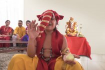Niño sentado vestido como Ganpati con modak en una mano y Ganpati ídolo en el fondo - foto de stock