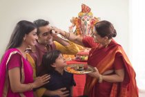 Familia india en ropa festiva celebrando ganesh chaturthi en interiores - foto de stock