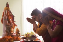 Муж и жена молятся с поднятыми руками перед идолом Ганеша — стоковое фото