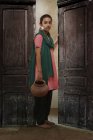 India chica con agua olla de pie cerca de casa puerta - foto de stock