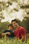 Sorrindo pai e filho sentado na grama no parque — Fotografia de Stock