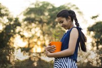 Низький кут зору усміхненої молодої дівчини тримає квітковий горщик в руці в парку — стокове фото