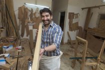Smiling carpenter in workshop checking straightness of wooden log — Stock Photo