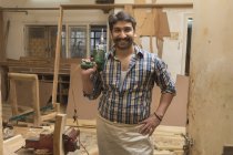 Carpintero sonriente posando con perforadora en taller - foto de stock
