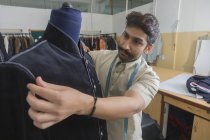 Tailor putting semi-stitched coat on mannequin in workshop to check fitting — Stock Photo