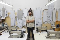 Улыбающийся портной, стоящий со скрещенными руками в мастерской швейными машинами — стоковое фото