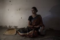 Mujer india sentada en el suelo en habitación débilmente iluminada - foto de stock