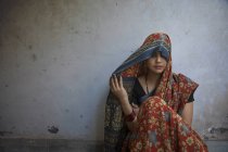 Mujer sonriente sentada en el suelo y cubriendo la cabeza con sari - foto de stock