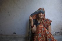 Smiling woman sitting on floor and covering head with sari — Stock Photo