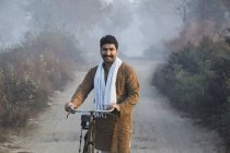 Agricultor masculino en carretera rural sosteniendo la bicicleta y mirando a la cámara - foto de stock