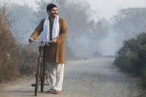Agriculteur masculin sur la route de campagne tenant vélo et regardant loin le matin brumeux — Photo de stock