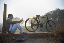 Фермер сидит рядом с сельскохозяйственным полем на велосипеде и пользуется мобильным телефоном — стоковое фото