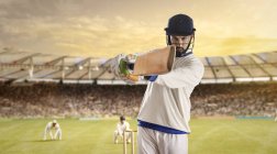 Joven deportista golpeando pelota mientras batea en el campo de cricket, enfoque selectivo - foto de stock