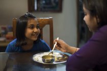 Young girl happily looks at her mother while she feeds her — Stock Photo