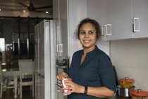 Jovem mulher de pé na cozinha e batendo café no copo . — Fotografia de Stock