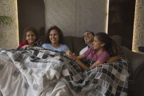 Familia feliz cómodamente sentado en el sofá debajo de una manta en casa . - foto de stock