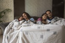 Счастливая семья уютно сидит на диване под одеялом дома . — стоковое фото
