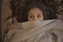 Young girl looking out surprisingly from under the blanket. — Stock Photo
