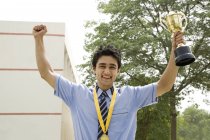 Student with arms raised and holding trophy triumphantly in the school yard — Stock Photo