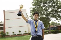 Estudante segurando um troféu triunfalmente no pátio da escola — Fotografia de Stock