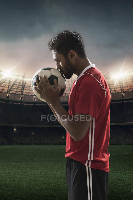 Joueur de football embrassant le football avec le stade en arrière-plan — Photo de stock