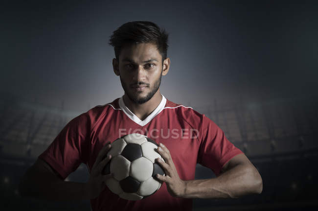 Giocatore di calcio che tiene il calcio con entrambe le mani con lo stadio sullo sfondo . — Foto stock