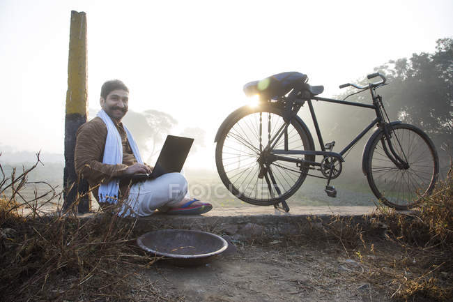 Agriculteur assis près du champ de l'agriculture et en utilisant un ordinateur portable — Photo de stock