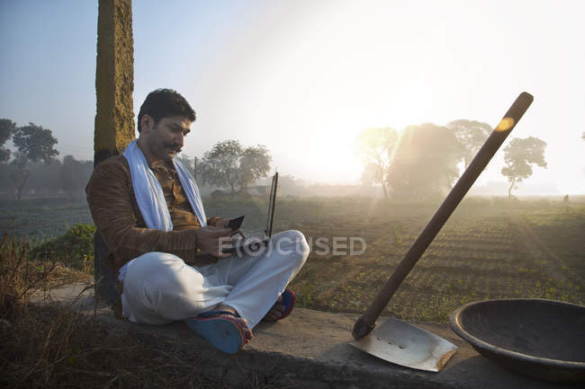 Agricultor sentado cerca del campo de la agricultura y el uso de ordenador portátil - foto de stock