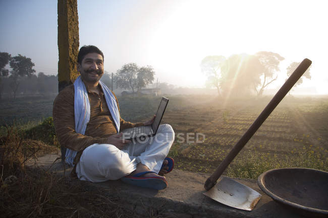 Landwirt sitzt in der Nähe von Ackerland und benutzt Laptop-Computer — Stockfoto