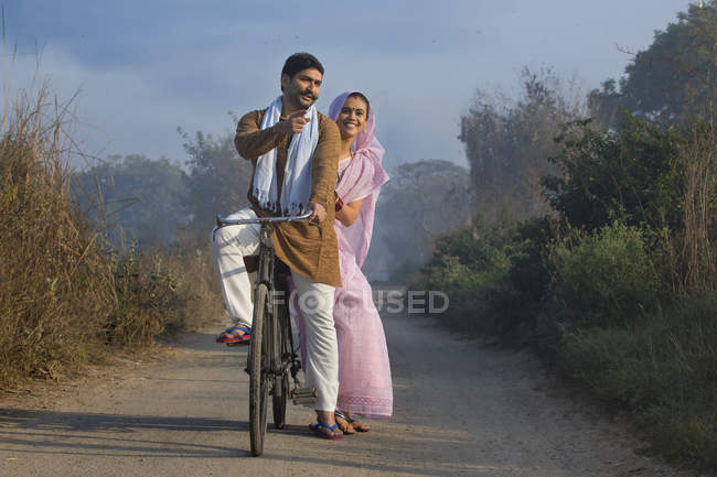Felice coppia rurale in abito tradizionale in bicicletta su strada di campagna — Foto stock