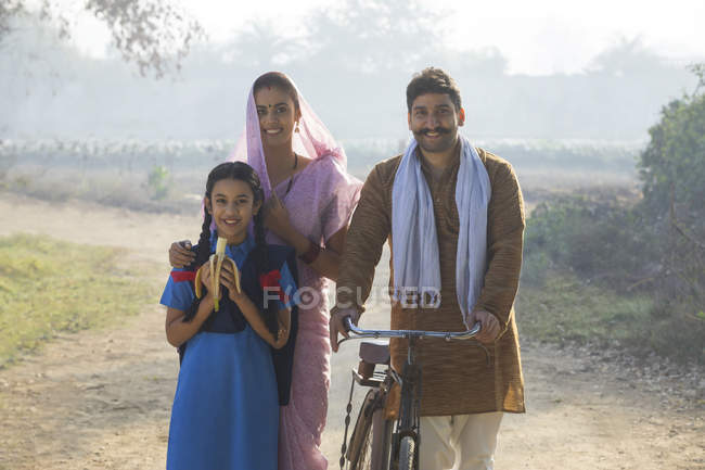 Счастливая сельская семья с велосипедом на деревенской улице — стоковое фото