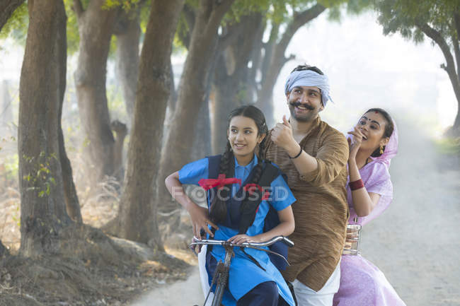Happy rural couple along with daughter riding on bicycle at village — Stock Photo