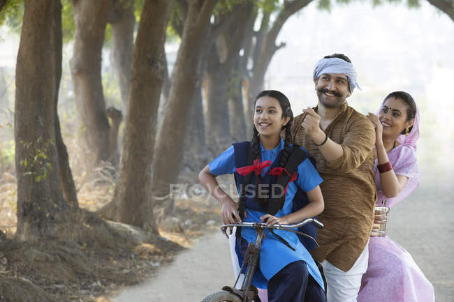 Счастливая сельская пара вместе с дочерью, катающейся на велосипеде в деревне — стоковое фото