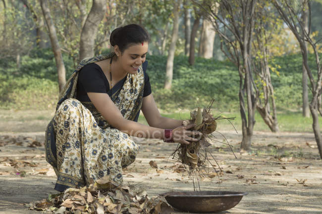 Mulher indiana vestida de sari coletando folhas secas do chão em ferro panela de ouro — Fotografia de Stock