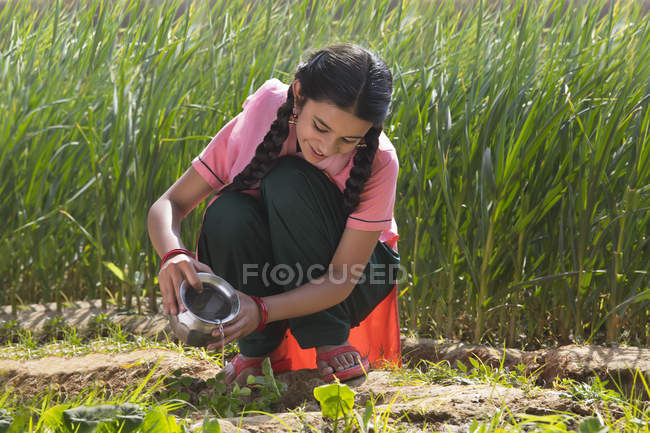 Menina indiana feliz regar pequenas plantas sentadas no campo agrícola — Fotografia de Stock