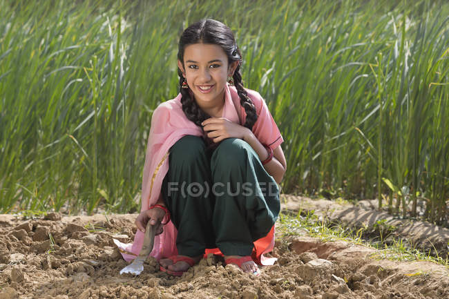 Piccola ragazza indiana scavare terreno utilizzando spatola seduta in campo agricolo — Foto stock