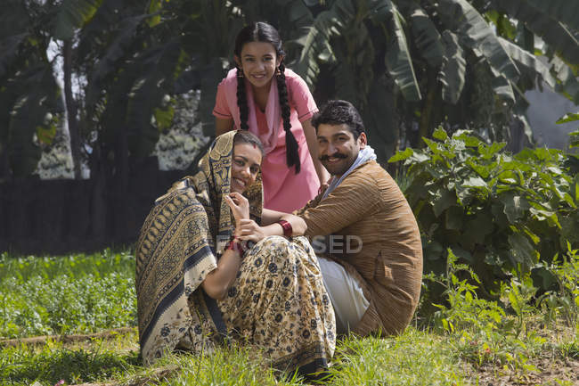 Sonriente familia india sentada en el campo agrícola - foto de stock